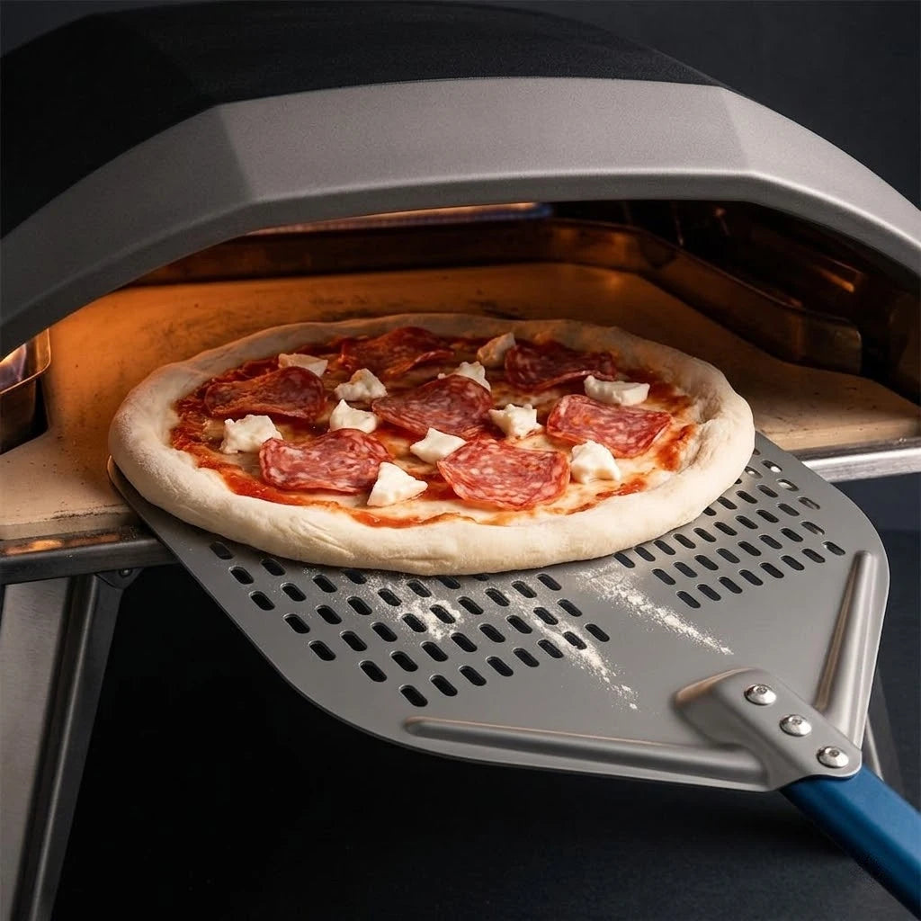 Pelle à pizza perforée en action : enfournement d’une pizza pepperoni dans un four à pizza professionnel.