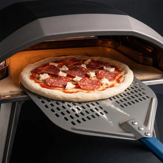 Pelle à pizza perforée en action : enfournement d’une pizza pepperoni dans un four à pizza professionnel.