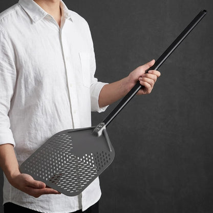 Homme présentant une pelle à pizza professionnelle perforée en aluminium gris avec long manche noir.